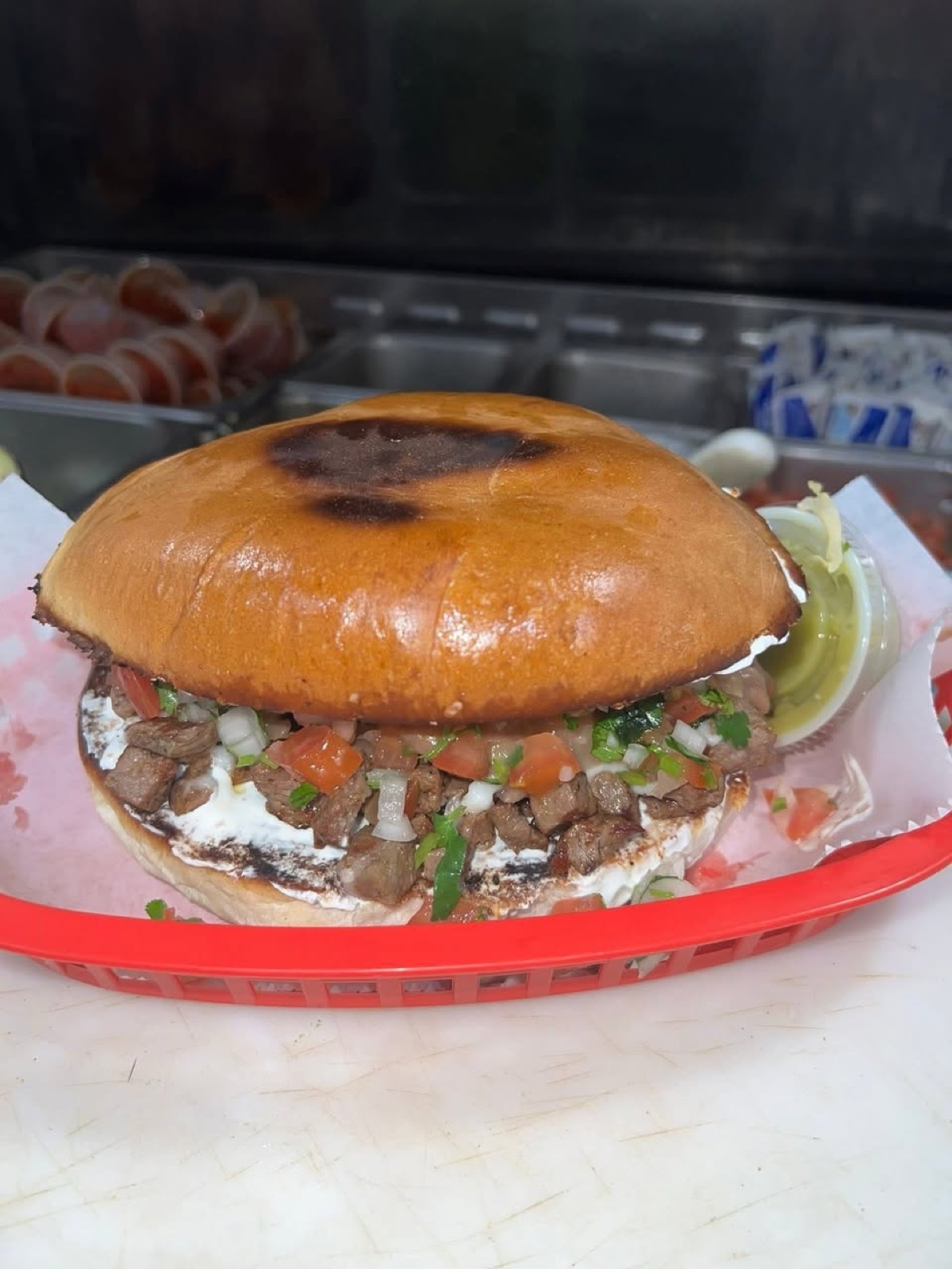A toasted torta on a telera roll stacked with carne asada, crema, pico de gallo and avocado in a basket