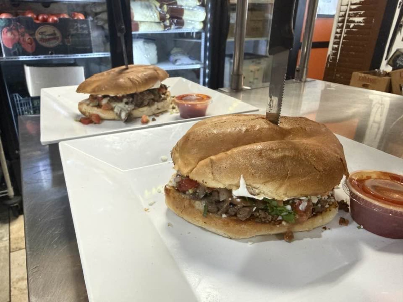 Two carne asada tortas plated at the counter, salsa on the side
